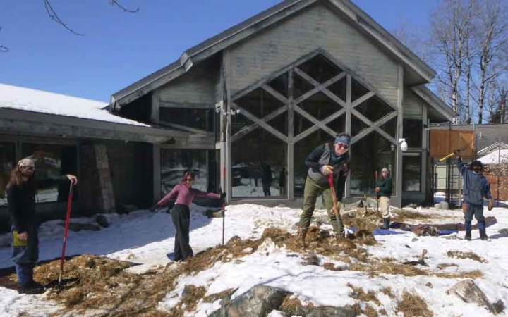 a group of students use tools to work on a piece of land in front of a building as part of a service project with outward bound